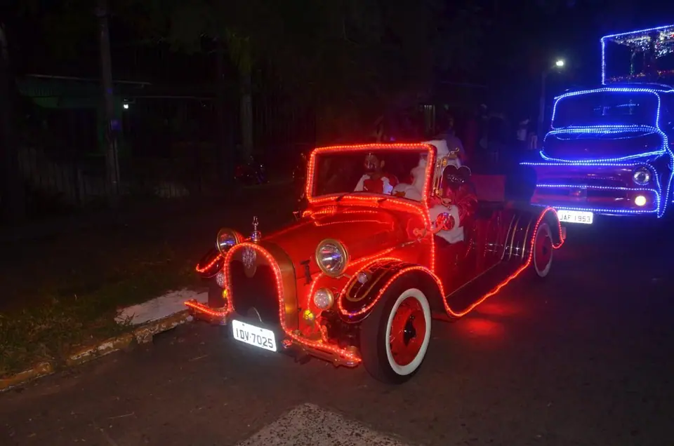 Calhambeque decorado com luzes vermelhas à noite, com um caminhão iluminado ao fundo
