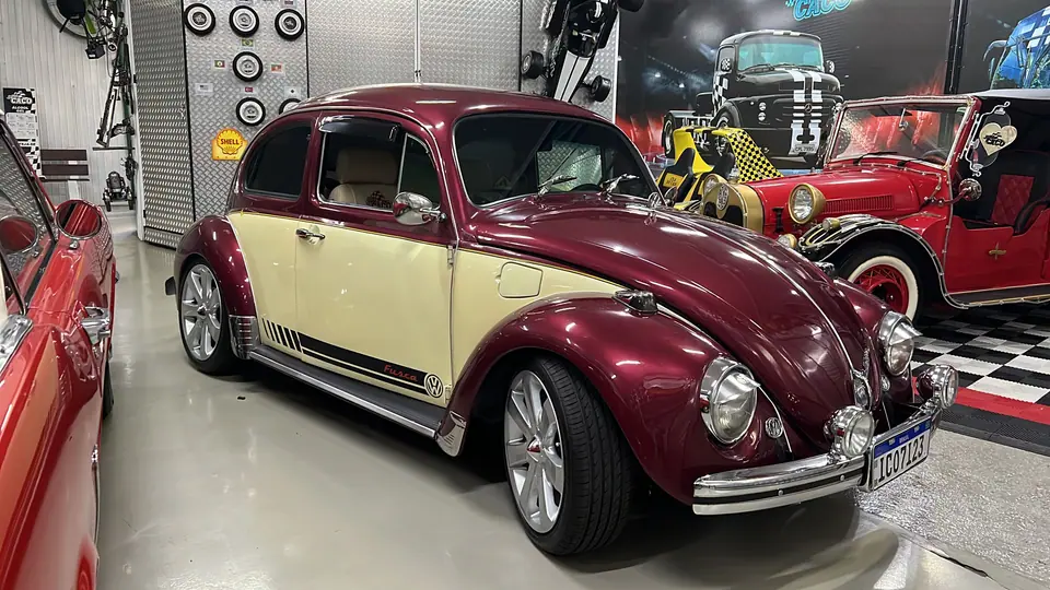 Fusca vinho e creme exposto em um galpão, visto de lado