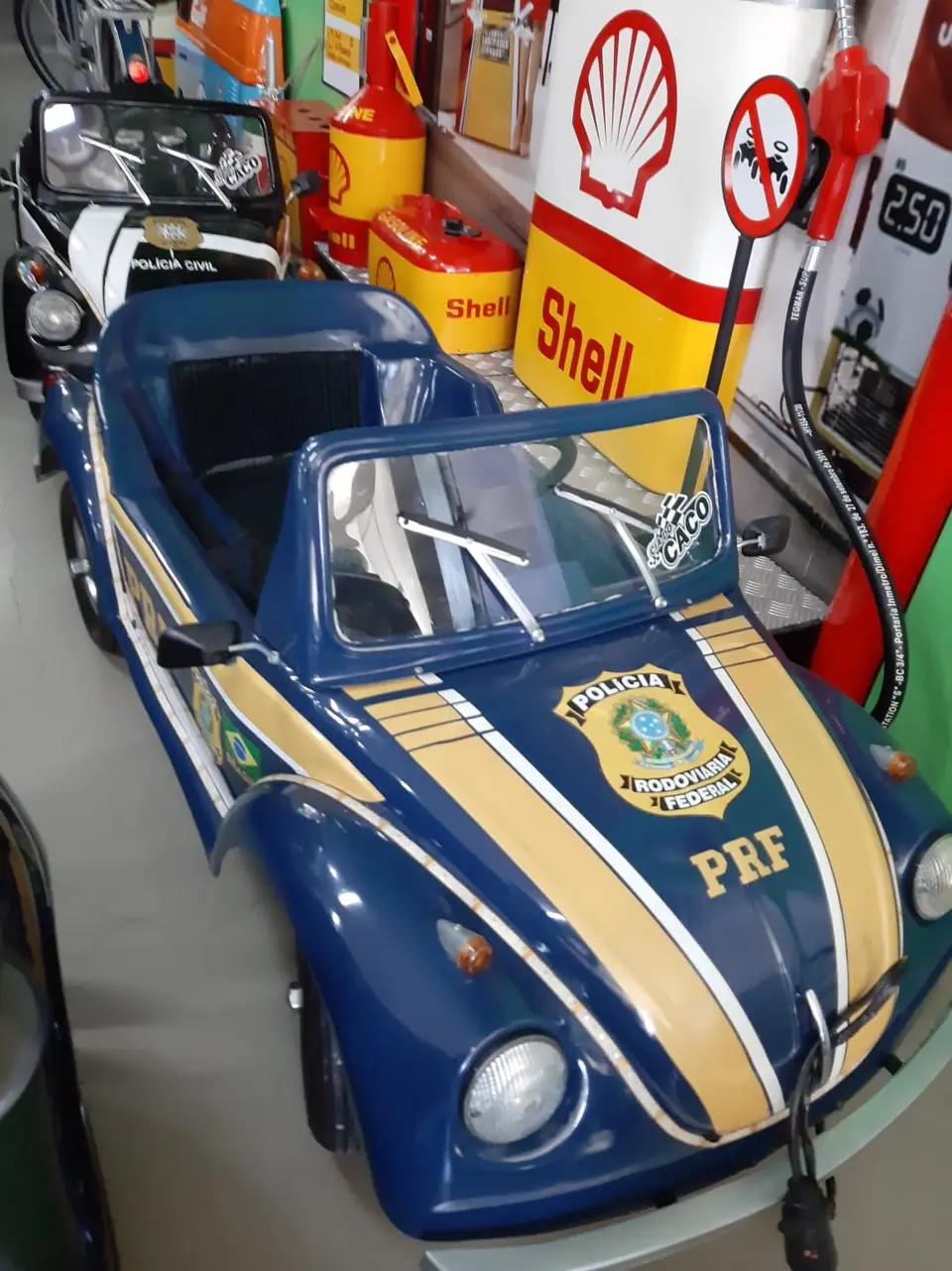 Mini Fusca azul da PRF diante de uma bomba de combustível Shell