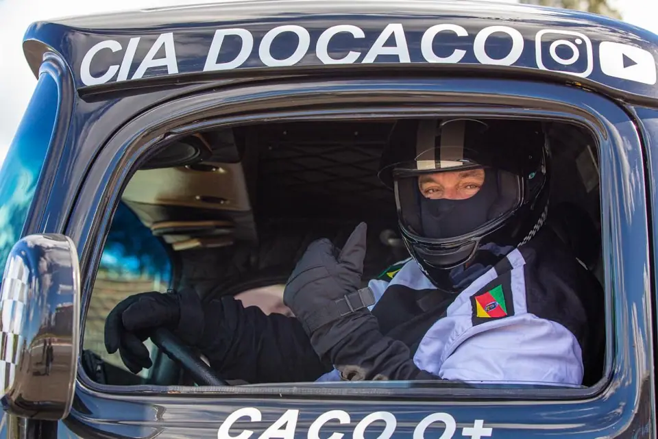 Piloto de capacete ao volante de um caminhão com a inscrição Cia do Caco