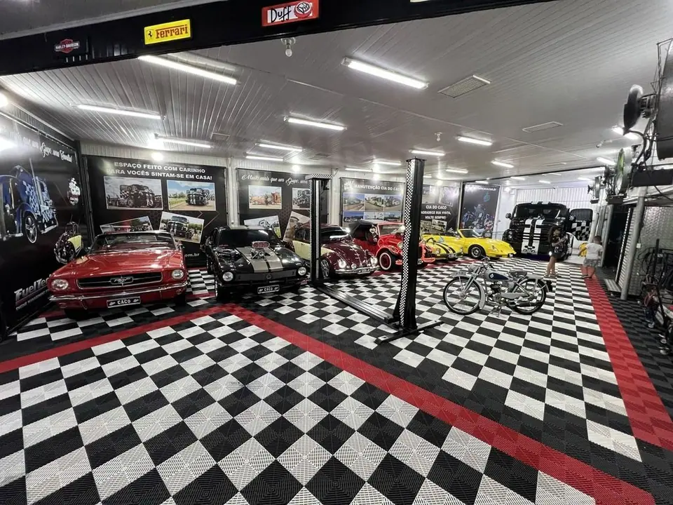 Galpão com carros sobre piso quadriculado preto, branco e vermelho