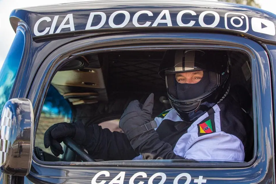 Piloto de capacete ao volante de um caminhão com a inscrição Cia do Caco