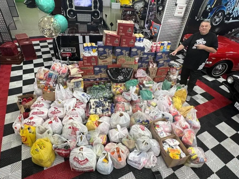 Doações de alimentos e brinquedos reunidas sobre o piso quadriculado da sede