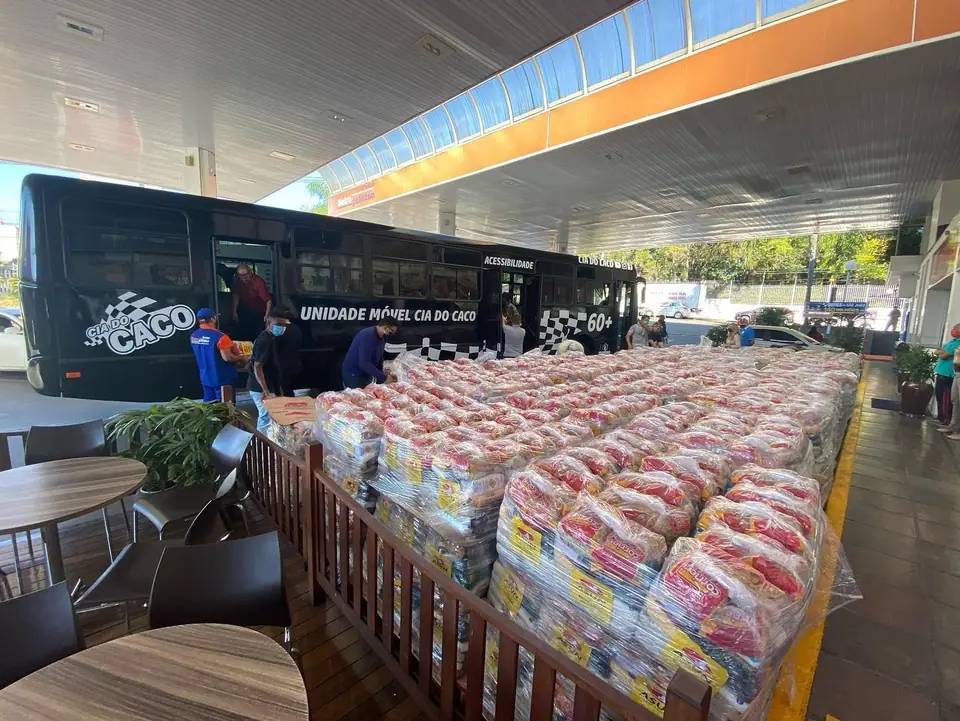 Centenas de cestas e sacolas de doação enfileiradas ao lado de um ônibus preto da Cia do Caco