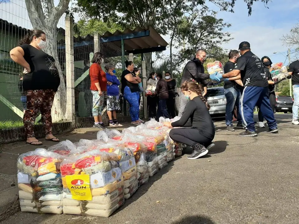Voluntários organizam fardos de alimentos na calçada, com pessoas aguardando