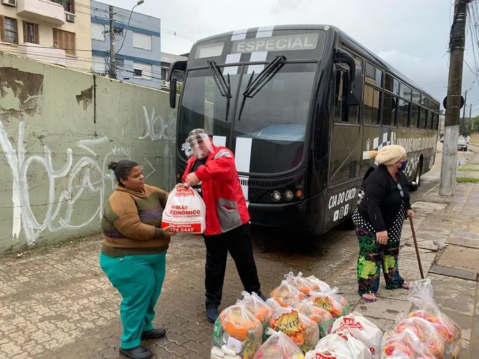 Voluntária entrega uma sacola a uma senhora ao lado de um ônibus preto