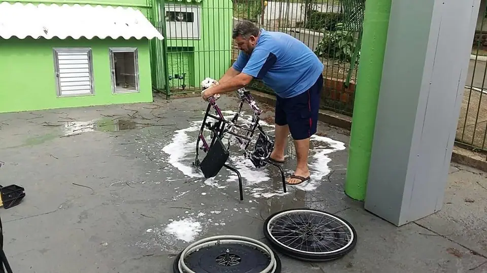 Homem lava uma cadeira de rodas em um pátio
