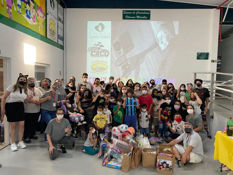 Grande grupo de crianças e adultos posando com presentes em um salão