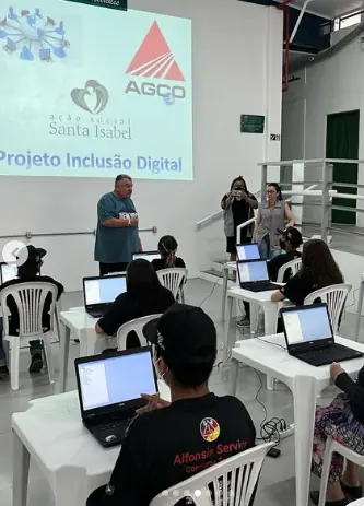 Crianças em computadores numa sala com a projeção Projeto Inclusão Digital
