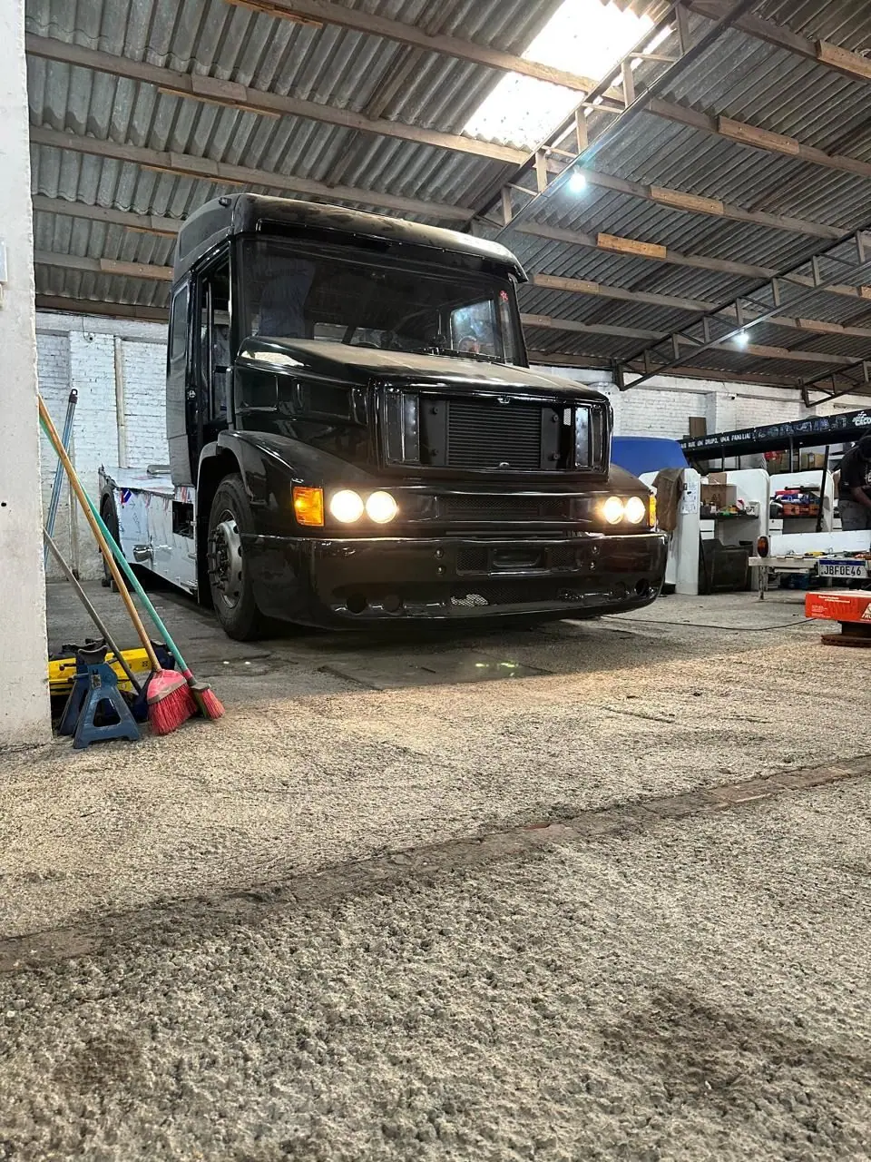 Caminhão Mercedes preto com os faróis acesos dentro da oficina
