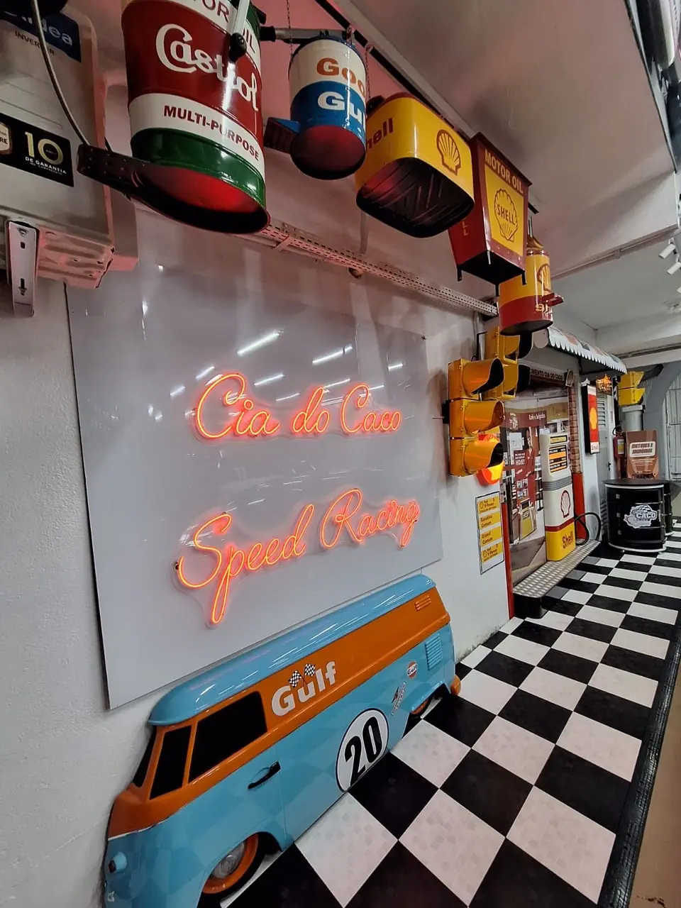 Parede com letreiro em neon da Cia do Caco Speed Racing e a frente de uma Kombi azul