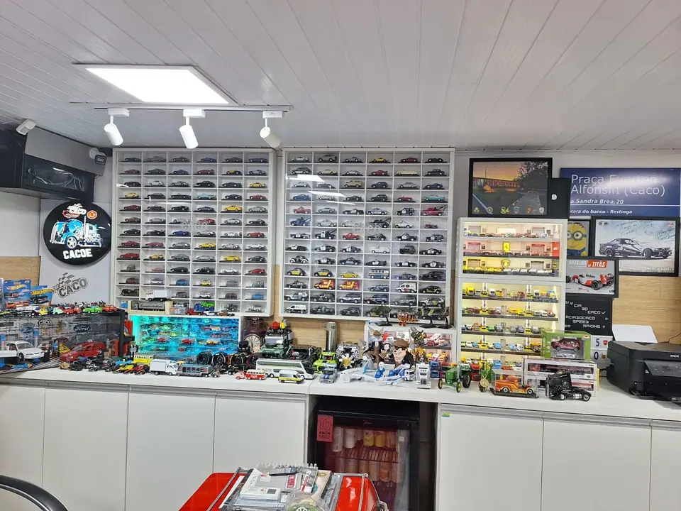 Bancada com miniaturas diante de uma parede de nichos com centenas de carrinhos