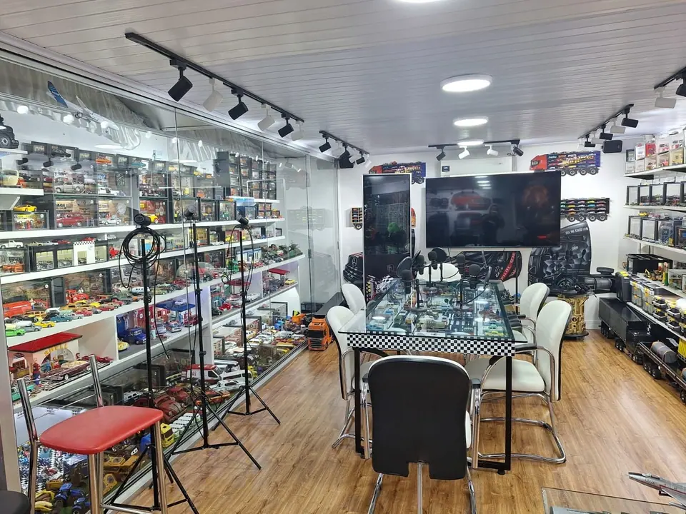 Sala com vitrines de miniaturas, mesa quadriculada e televisão ao fundo
